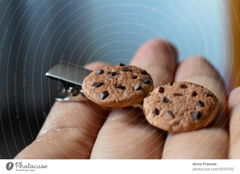 Hand hält eine handgefertigte Haarnadel mit Miniatur-Tonkeks Polymer Haarspange Makro Nahaufnahme Handwerk Kunst Cookies Schokoladenstückchen realistisch