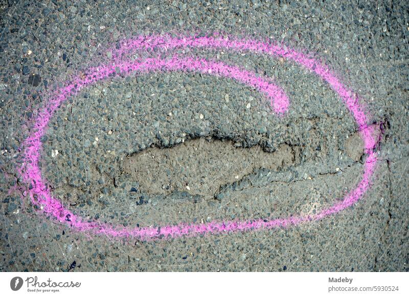 Mit einem schwungvoll handgemalten Kreis in Lila markiertes tiefes Schlagloch in grauem Asphalt im Sommer bei Sonnenschein in Hafenweg in Münster in Westfalen im Münsterland