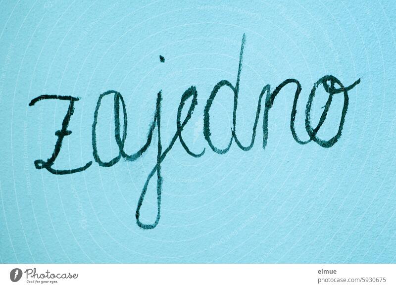 zajedno (gemeinsam) in schwarzer Handschrift an einer blauen Wand kroatisch miteinander zusammen Schreibschrift Zusammensein Zusammenhalt Teamwork Freundschaft