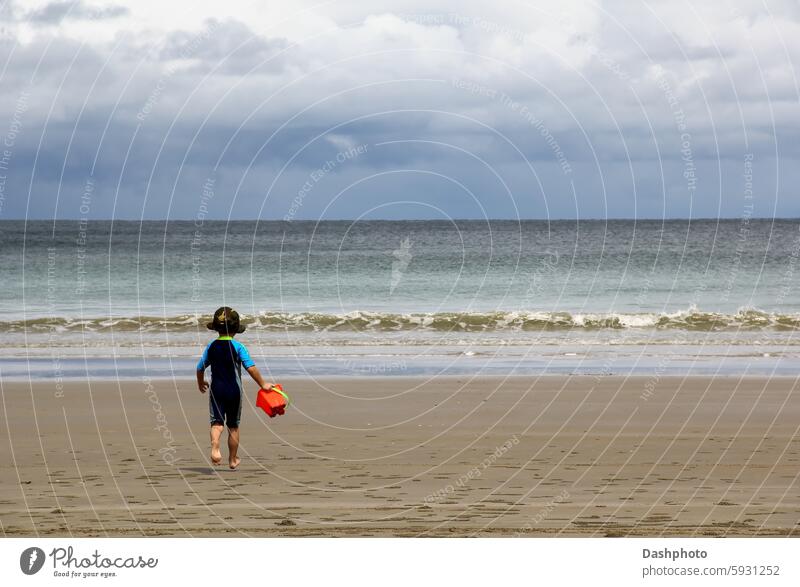 Kleiner Junge läuft an einem tropischen Strand auf das Meer zu klein kleiner Junge Kind Kleinkind Hut Sonnenhut Badeanzug Eimer laufen rennen Sand MEER