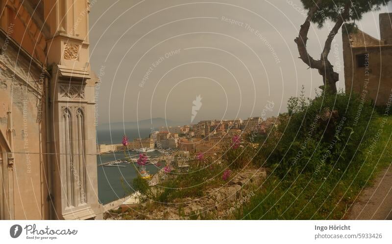 Links ein Teil der Kathedrale von Gaeta (Italien) Rechts ein altes Gebäude und die Silhouette einer Schirmpinie. Dazwischen der Blick auf die Altstadt und den Hafen von Gaeta.