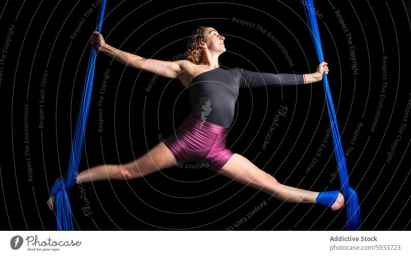 Lufttänzerin mit blauer Seide vor schwarzem Hintergrund Frau Antenne Tanzen Seiden Flexibilität Stärke dynamisch Split Pose vereinzelt schwarzer Hintergrund