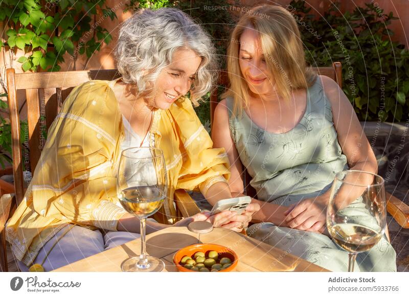 Zwei Frauen, die einen gemütlichen Nachmittag mit Wein im Freien verbringen reif Senior Freundschaft Freizeit trinken Garten Tisch Glas Sommer Smartphone