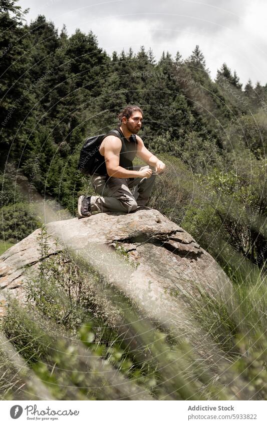 Mann, der auf einem Felsen sitzend über die Natur nachdenkt Wald im Freien Wanderer Kontemplation Grün ernst muskulös Rucksack Sitzen Abenteuer sportlich