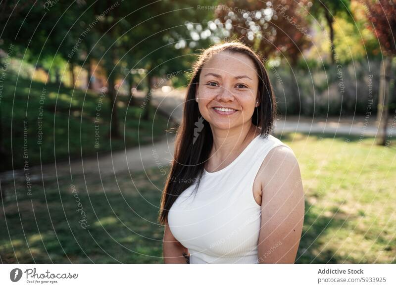 Porträt einer lächelnden kolumbianischen Frau, die einen sonnigen Tag in einem üppigen grünen Park genießt Lächeln Baum im Freien Natur Glück Sommer hell lässig