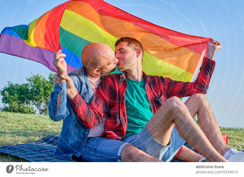 Ein schwules Paar drückt seine Liebe unter einer Flagge im Freien aus Stolz Fahne Kuss Mann Zuneigung Partnerschaft abstützen Regenbogen Emotion romantisch