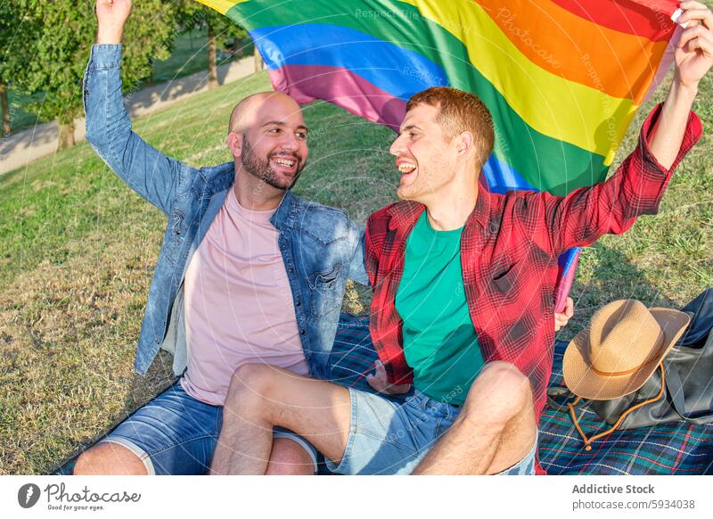 Schwules Paar feiert mit Regenbogenfahne im Park schwul Fahne Picknick Decke Feier Stolz Freude Lächeln Fröhlichkeit männlich Liebe Partnerschaft im Freien