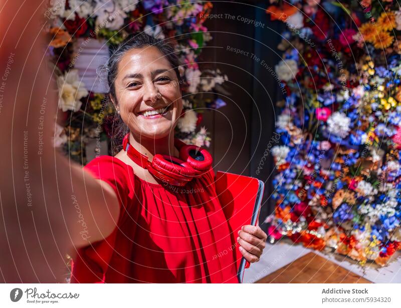 Glückliche Frau in Rot, die ein Selfie mit einem blumigen Hintergrund macht rot Lächeln geblümt farbenfroh Laptop Kopfhörer Hals pulsierend Outfit Blume Anzeige