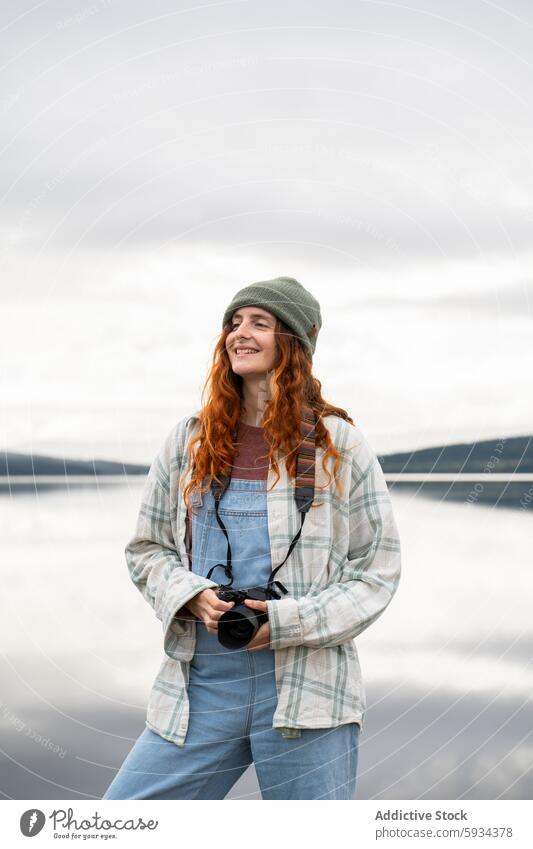 Rothaarige Frau genießt die Natur beim Camping im Freien Fotokamera See Lächeln rote Haare wolkig lässig Kleidung freudig malerisch Seeufer Abenteuer reisen