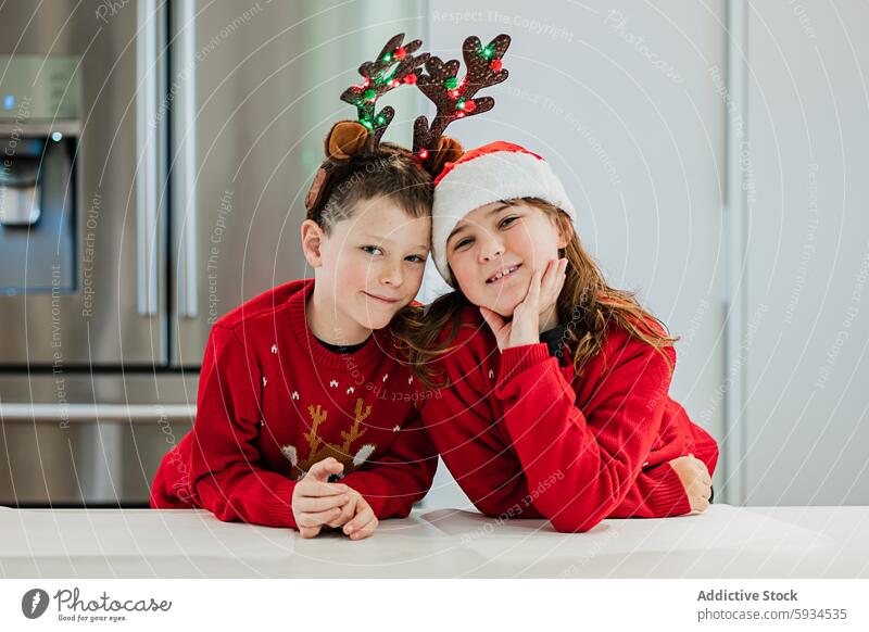 Zwillingsgeschwister in festlichen Outfits feiern gemeinsam Weihnachten Geschwisterkind Junge Mädchen Pullover Rentier Geweih Weihnachtsmann Hut Lächeln freudig