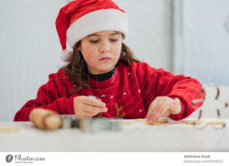 Junges Mädchen backt Plätzchen in festlichem Weihnachtsoutfit Weihnachten backen Keks Feiertag Weihnachtsmütze roter Pullover Küche Aktivität Konzentration