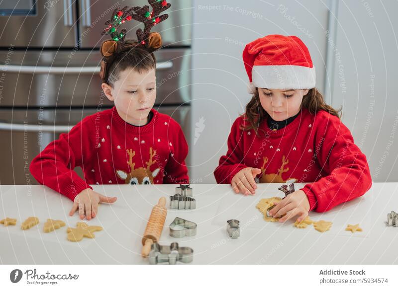 Zwillinge backen Weihnachtsplätzchen in festlichen Outfits Kind Weihnachten Keks Feiertag Pullover Hut Küche modern Konzentration heiter saisonbedingt Szene