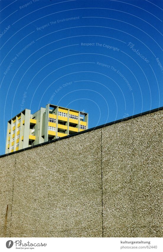 Berliner Plattenbau hinter einer Mauer Osten Stadt Beton gelb Haus Hochhaus Balkon diagonal blau Himmel unteransicht