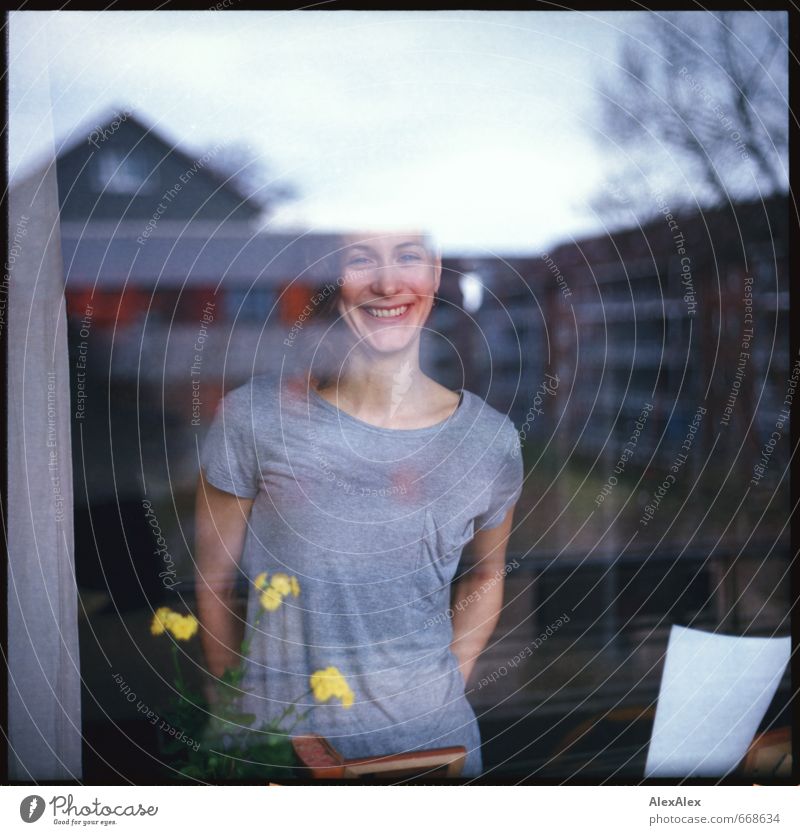 analoges Portrait eine jungen, lächelnden Frau hinter einer Fensterscheibe Junge Frau Jugendliche Kopf Grübchen 18-30 Jahre Erwachsene Blume Mehrfamilienhaus
