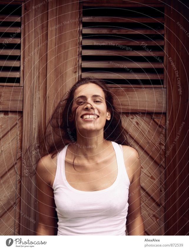 Junge Frau vor einer Holztür schwenkt lachend ihr langes Haar Jugendliche 18-30 Jahre Erwachsene Unterhemd schwarzhaarig langhaarig Bewegung Lächeln ästhetisch