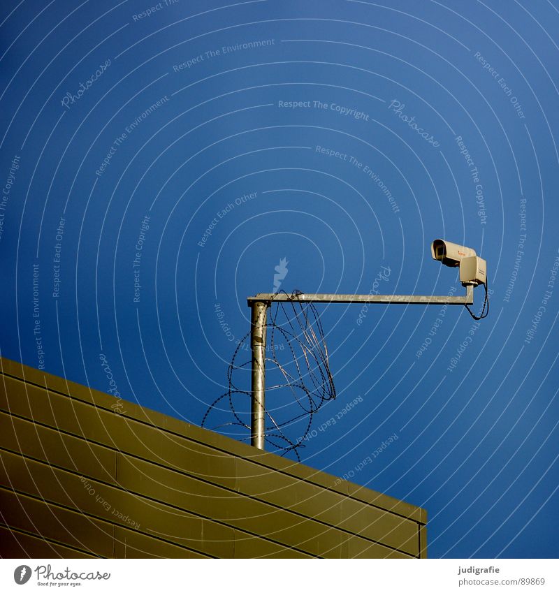 Auge Überwachungskamera beobachten Sicherheit Haus Gebäude Dach Stacheldraht Verkehrswege Detailaufnahme Fotokamera Überwachungsstaat Schutz Himmel blau