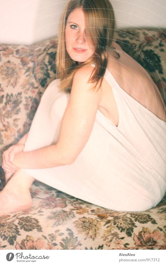 Junge Frau in Unterhemd sitzt auf einer geblümten Couch und schaut seitlich in die Kamera Sofa Raum Nachtleben Jugendliche Gesicht Rücken Sommersprossen