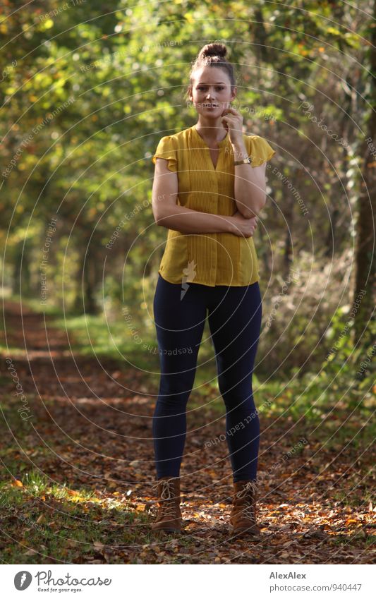 Junge Frau in gelbem Top und Jeans steht vor einem mit von Bäumen gesäumten Weg Ausflug wandern Jugendliche 18-30 Jahre Erwachsene Landschaft Schönes Wetter