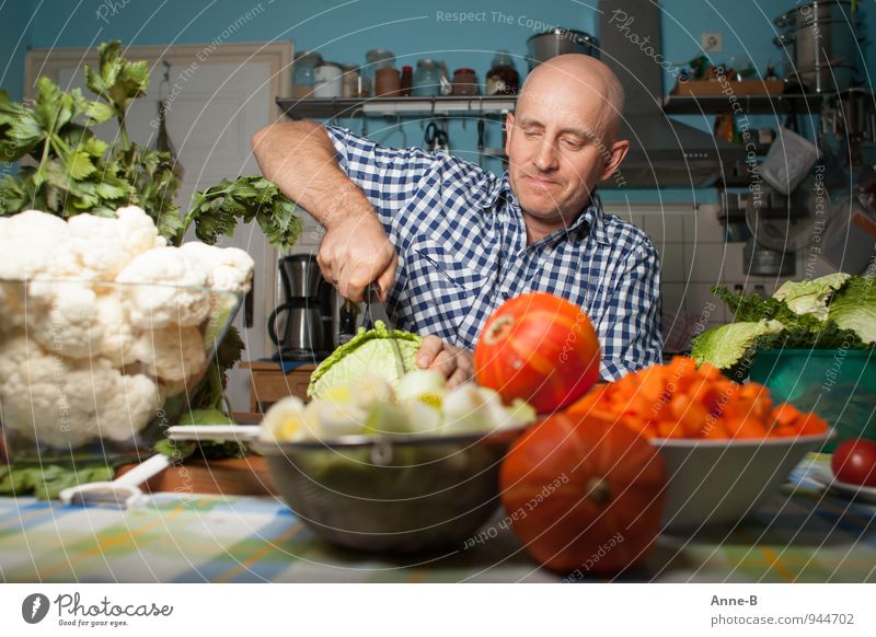 Ein Mann im Karohemd schneidet einen Wirsing in der Küche. Um ihn herum auf dem Tisch ist viel Gemüse. Suppe Eintopf Vegetarische Ernährung Geschirr Gesicht