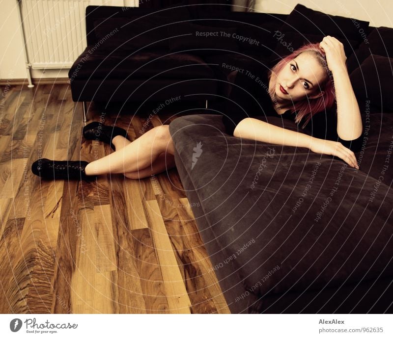 Junge Frau mit pinken Haaren liegt auf die Couch gelehnt Wohnung Sofa Wohnzimmer Holzfußboden Nachtleben Jugendliche Beine 18-30 Jahre Erwachsene T-Shirt