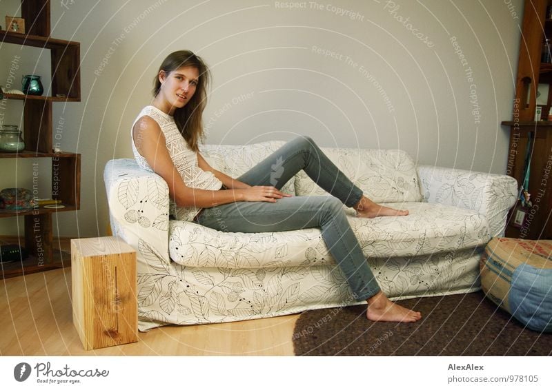junge, große, langbeinige Frau sitzt barfuß auf einer hellen Couch Wohnung Sofa Wohnzimmer Junge Frau Jugendliche Beine Barfuß 18-30 Jahre Erwachsene Jeanshose